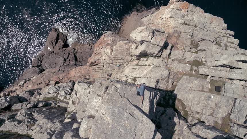 A man climbs up a rocky mountain on a coast