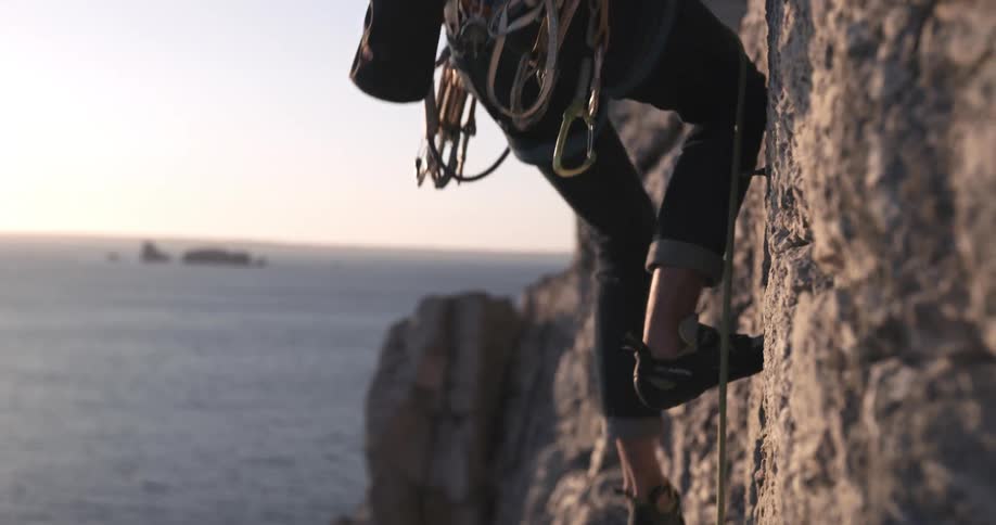A rock climber goes up a cliff over the ocean