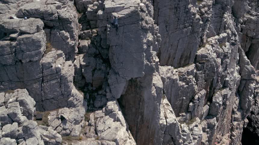 A person is climbing a rock on a broken mountain and at the base there is a stream running through it