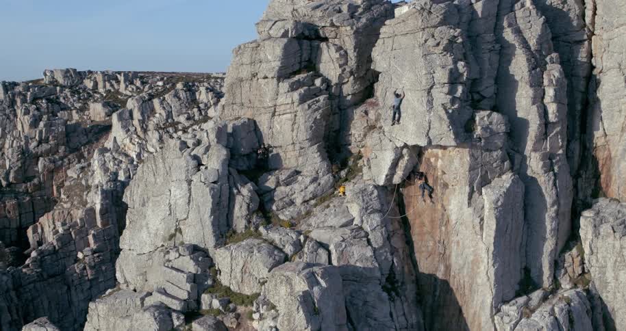 Trio of rock climbers climb rocky cliff face of rugged mountain