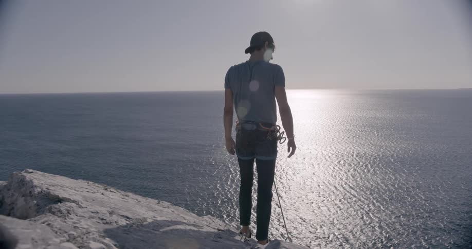 Man getting up and standing on a mountain peak with a seat belt and by the sea