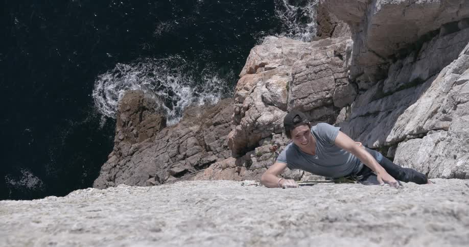 A person is climbing a rocky cliff above the sea