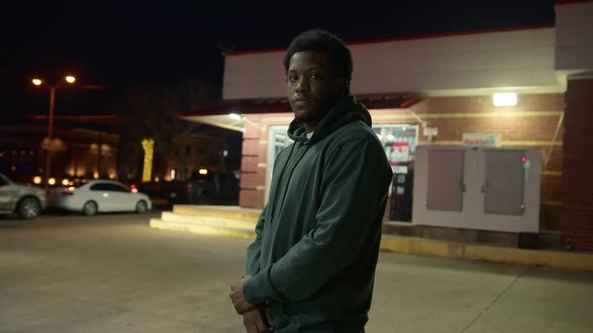 A black man stands outside a gas station