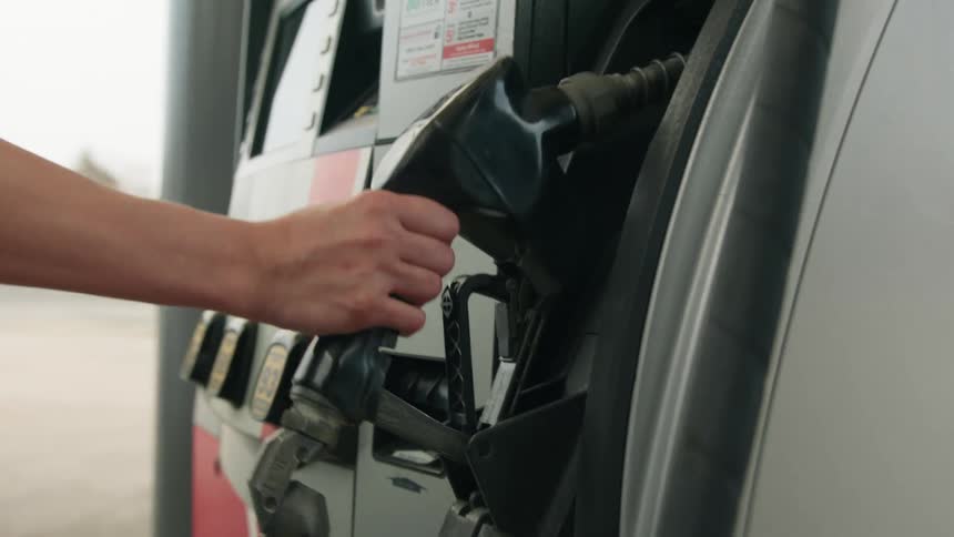 Hands of a person picking up the valve on a pump at the gas station during the day