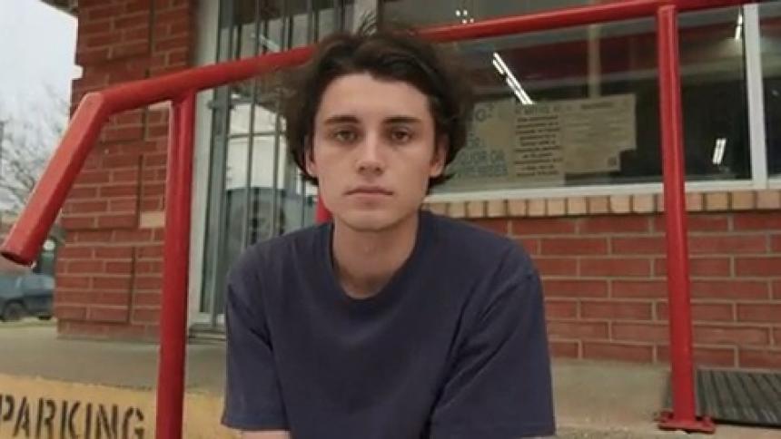 A teenage boy sits outside a gas station
