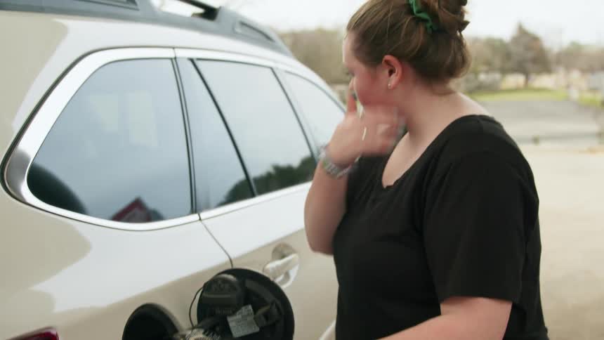 A woman primps her hair while pumping gas