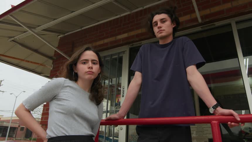 Man and woman lean against rail outside convenience store