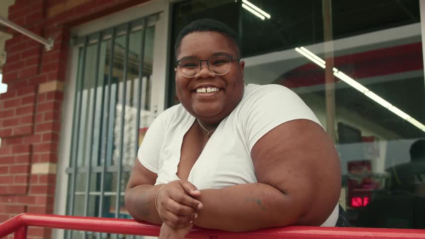 Portrait of a young woman smiling while resting her arms on a handrail outside an establishment