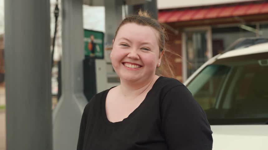 A young woman laughs outside a gas station