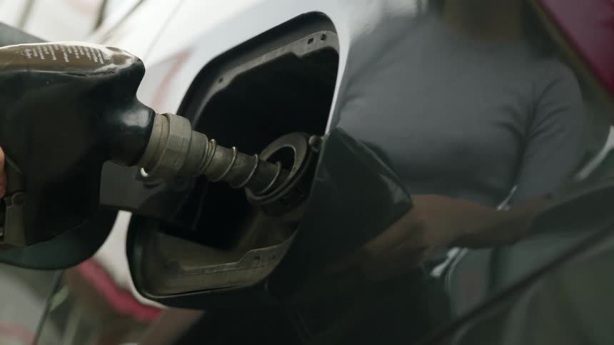 Womans hand placing the fuel valve on the tank of her vehicle and refueling her car