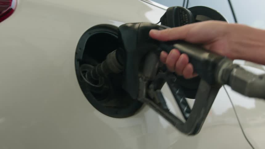 A woman puts a gas pump handle into a car