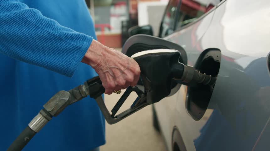 Closeup on an elderly ladys hands and putting the valve on the gas tank and her vehicle and filling up