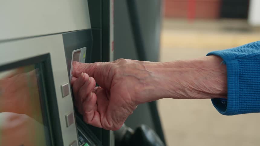An elderly woman uses a card reader on a gas pump