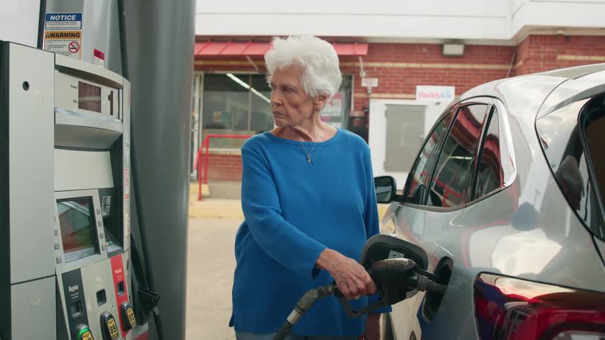An elderly woman is at the gas station filling up her vehicle