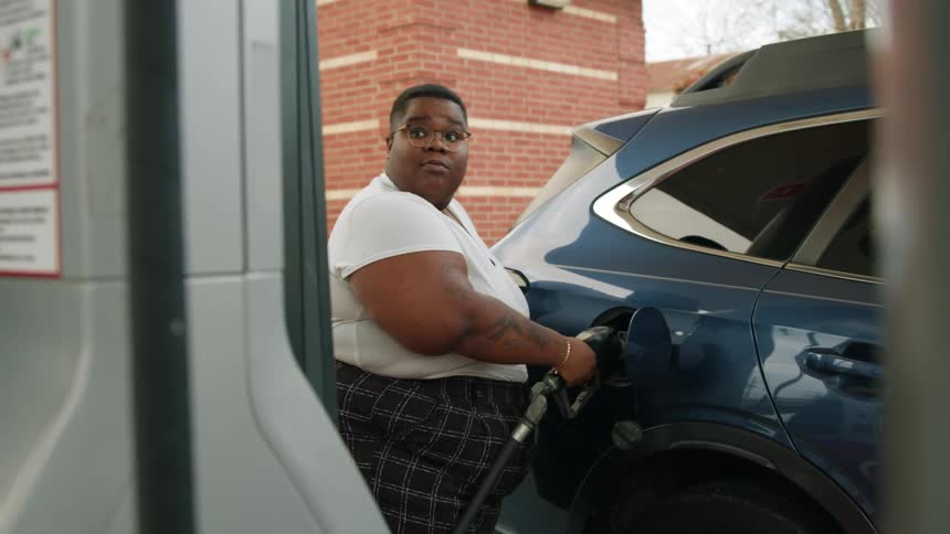 Woman places gas pump in gas tank inlet and looks back at the screen