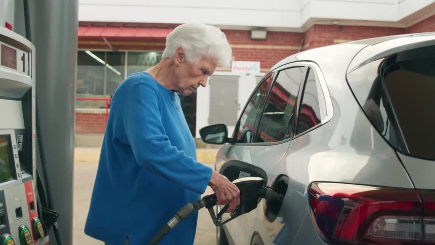 Elderly lady at the gas station putting the valve on her vehicles fuel tank and filling up