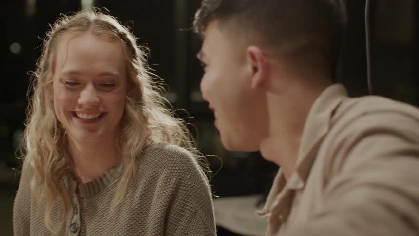 Friends provide food to woman while they eat together at a restaurant at night