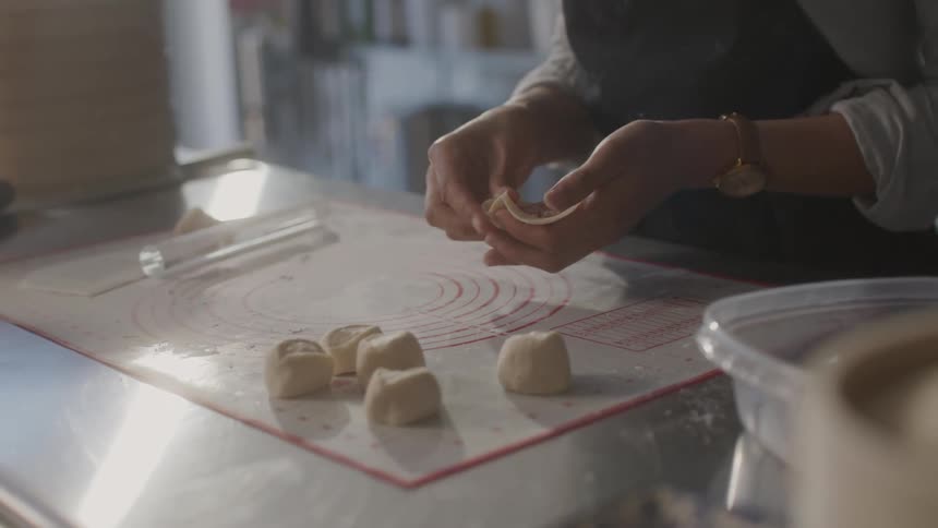 Closeup of a womans hands placing raw meat into dough and closing dumplings