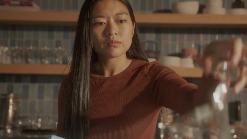 Young woman drying crystal glasses and glasses and placing on a shelf in a restaurant