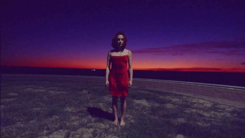 A female dancer stands still before performing her red dress blowing in the wind