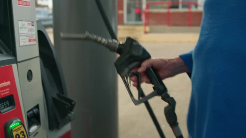 Hands of an elderly lady removing the fuel filler valve from her car and returning it to the pump at the gas station
