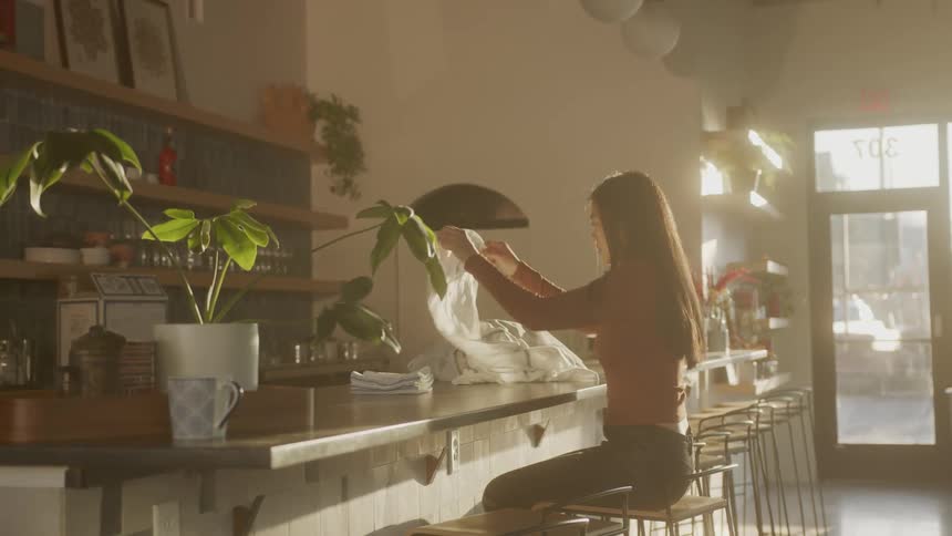 Woman inside a restaurant sitting at a counter folding cloths