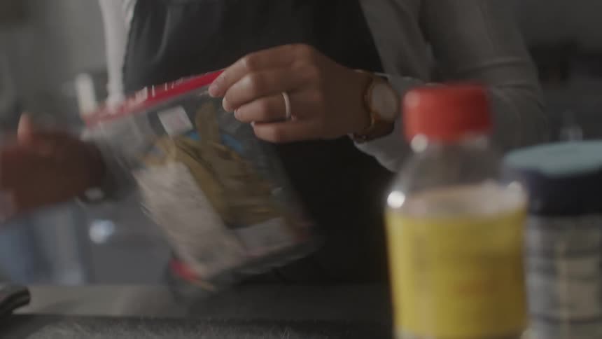 Woman with a black apron in a kitchen removing dry spice leaves and placing them on a counter