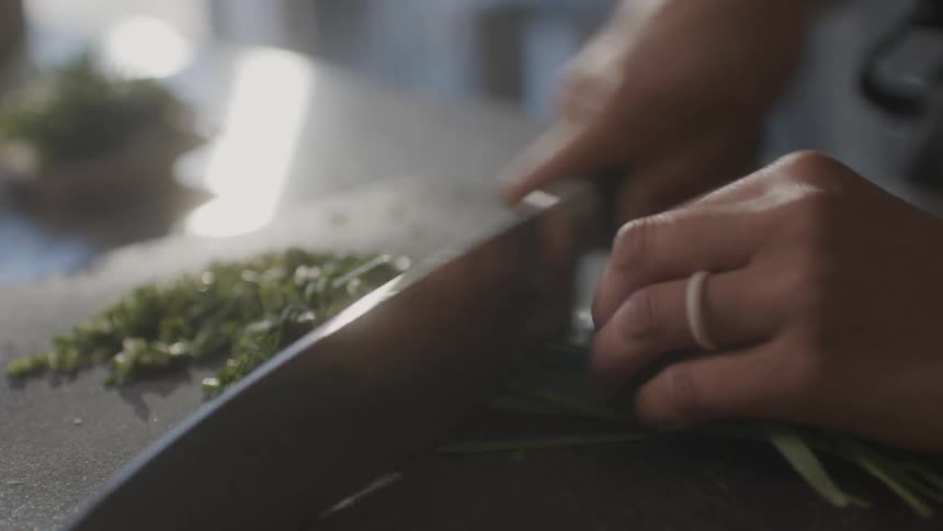 Closeup of a womans hands with a knife cutting chives on a table