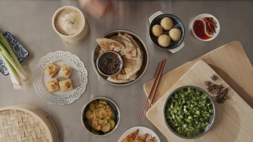 A persons hands placing seasoned vegetables on a table with asian food presentation