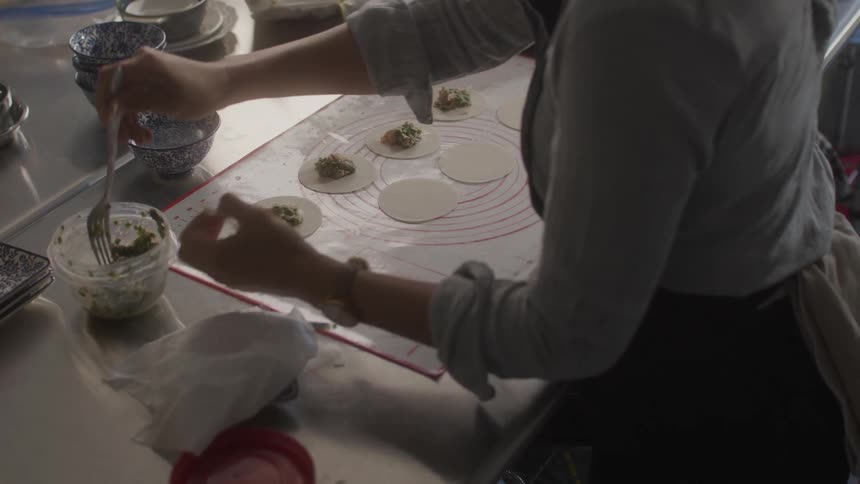A womans hands with the help of a fork placing ingredients into a small round dough