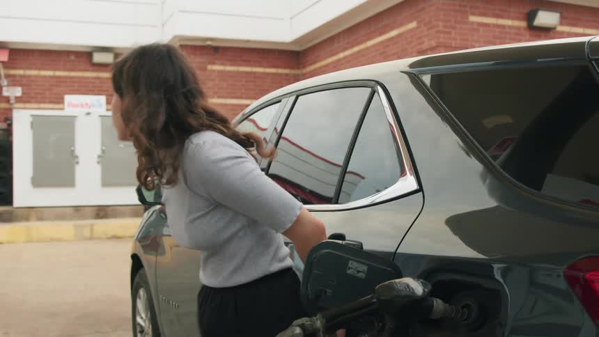 Woman leans against vehicle after placing gas pump into tank at gas station