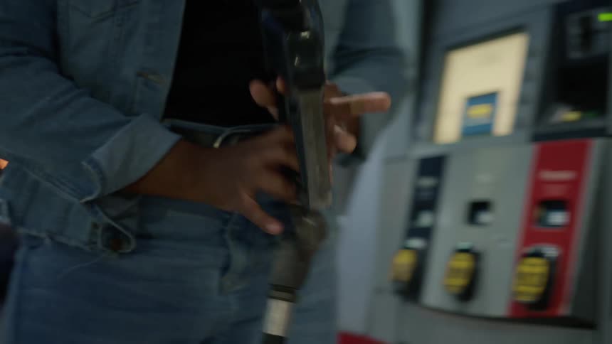 A young woman removes a gas pump nozzle from her vehicle placing it back in the gas pump