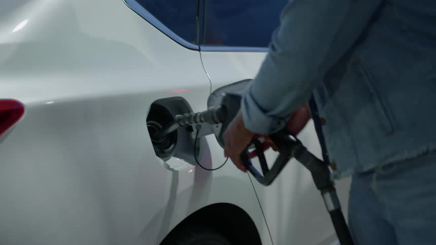 Closeup of a womans hands reaching for the valve on a fuel pump and filling up her car
