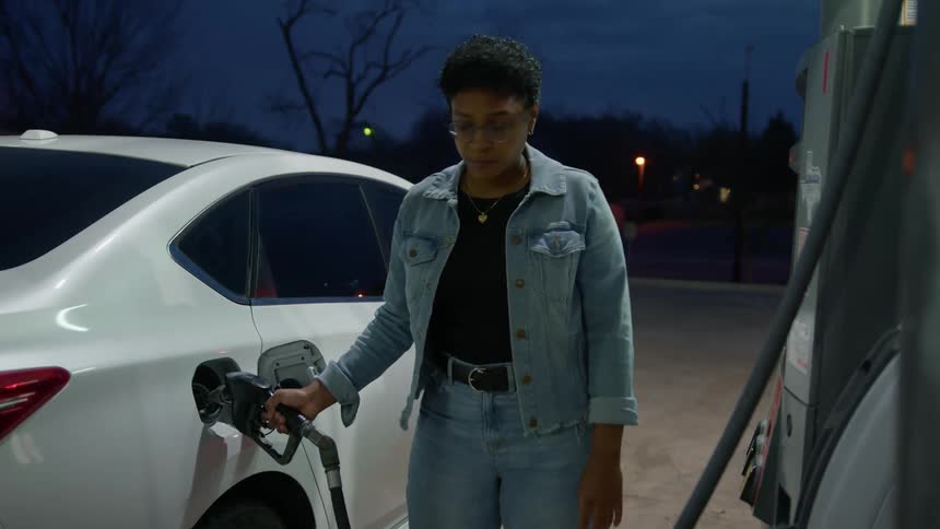 Woman puts gas in her car at sunset