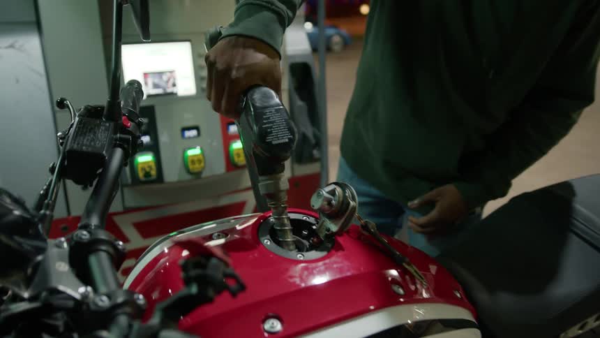 Man at a gas station at night refueling his motorcycle