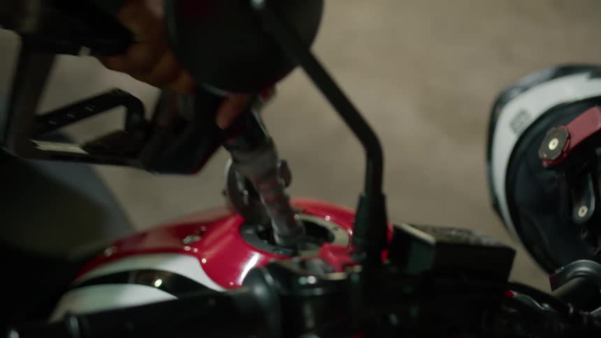 Person wearing long sleeved shirt fills motorcycle gas tank at gas station