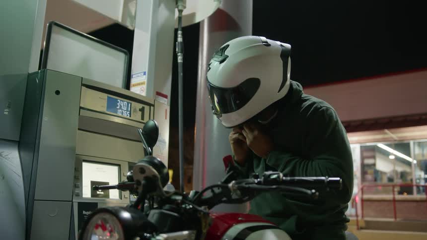 A man riding a motorcycle up to a gas station pump