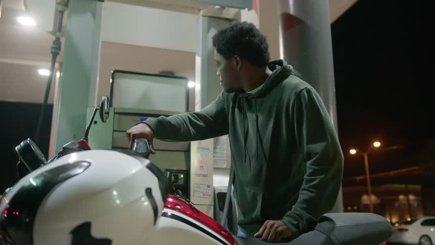 A young man at a gas station pumping gas into his motorcycle at night