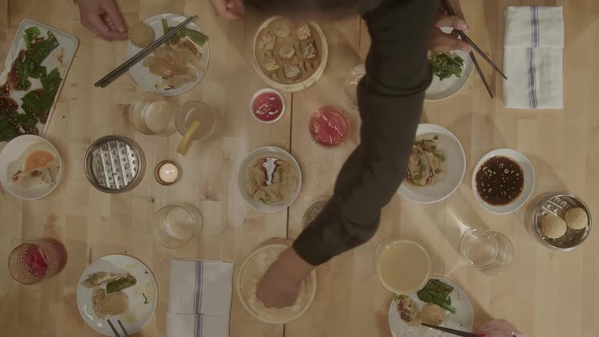 View of a table with peoples hands holding chopsticks and eating asian cuisine with wooden bowls and steamed dumplings