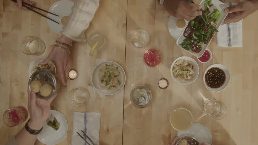Four people pass platters to each other and use chopsticks to put food from each on their plates