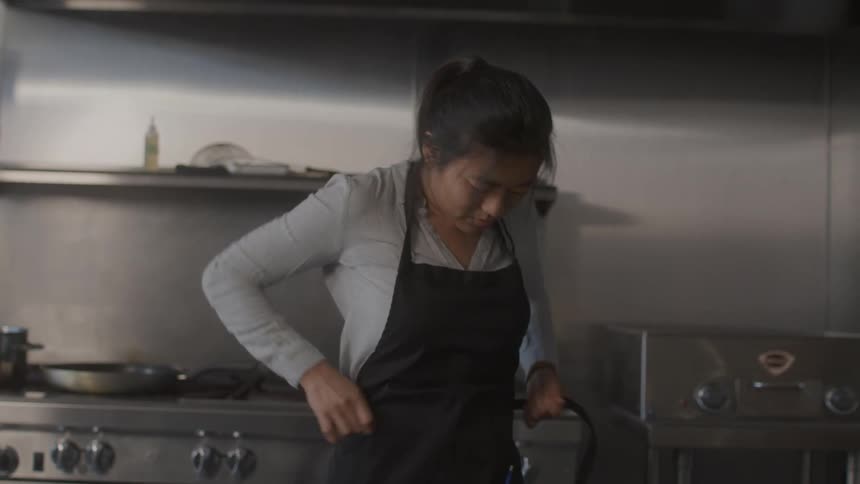 A woman puts on an apron as she prepares to cook a meal