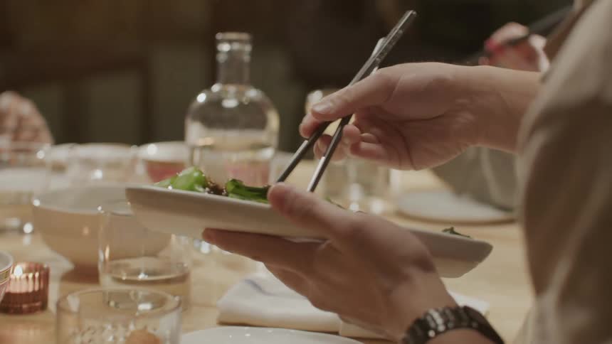 People sitting at a table pass around dishes and use chopsticks to put food on their plates