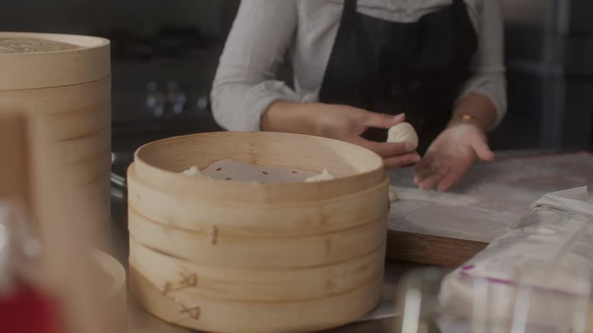 A womans hands preparing nikuman dumplings and placing them inside a wooden bowl