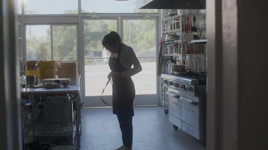 Woman entering a kitchen with a steam bowl and then putting on her apron