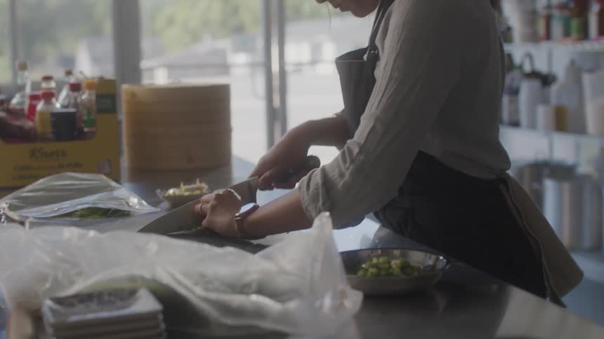 Young man and asian woman in a kitchen and with a knife cutting chives
