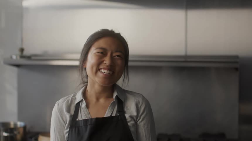Portrait of a young asian woman smiling and wearing a black apron in the kitchen