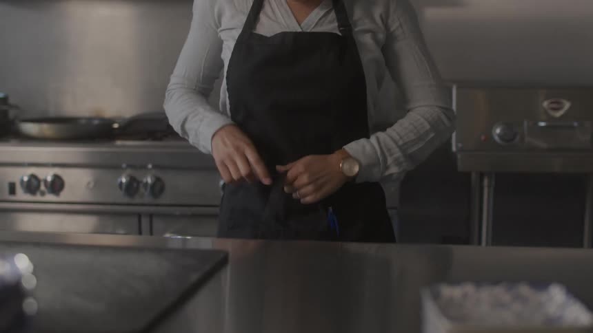 An asian woman puts on an apron in a kitchen