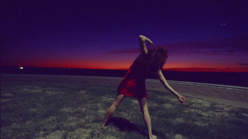 Redhead woman dancing on a lawn outdoors at night with red sky