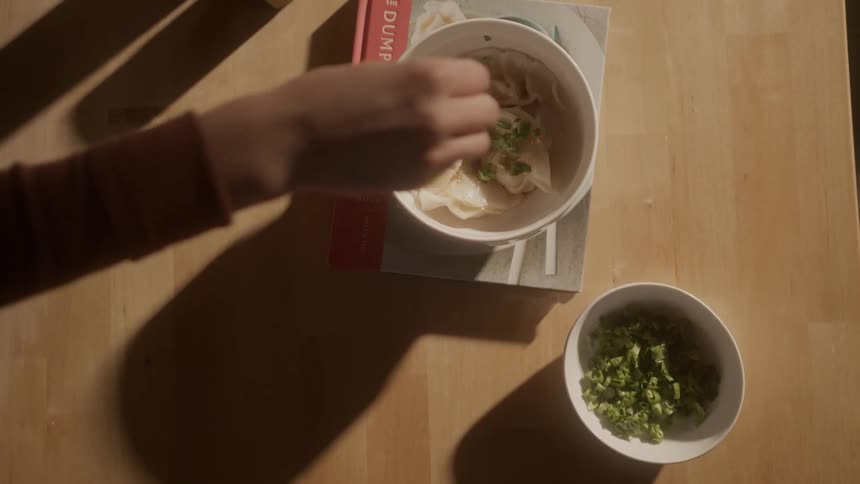 A person sprinkles garnish on the dumplings
