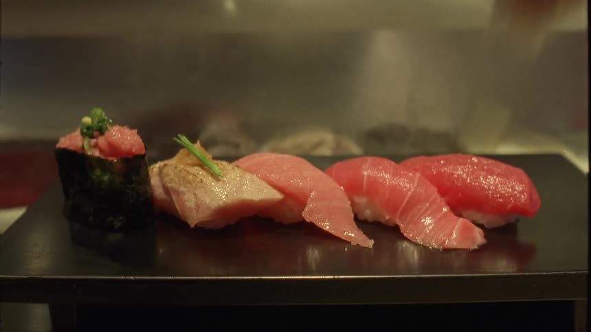 A sushi chefs hand placing ginger on a plate of sushi